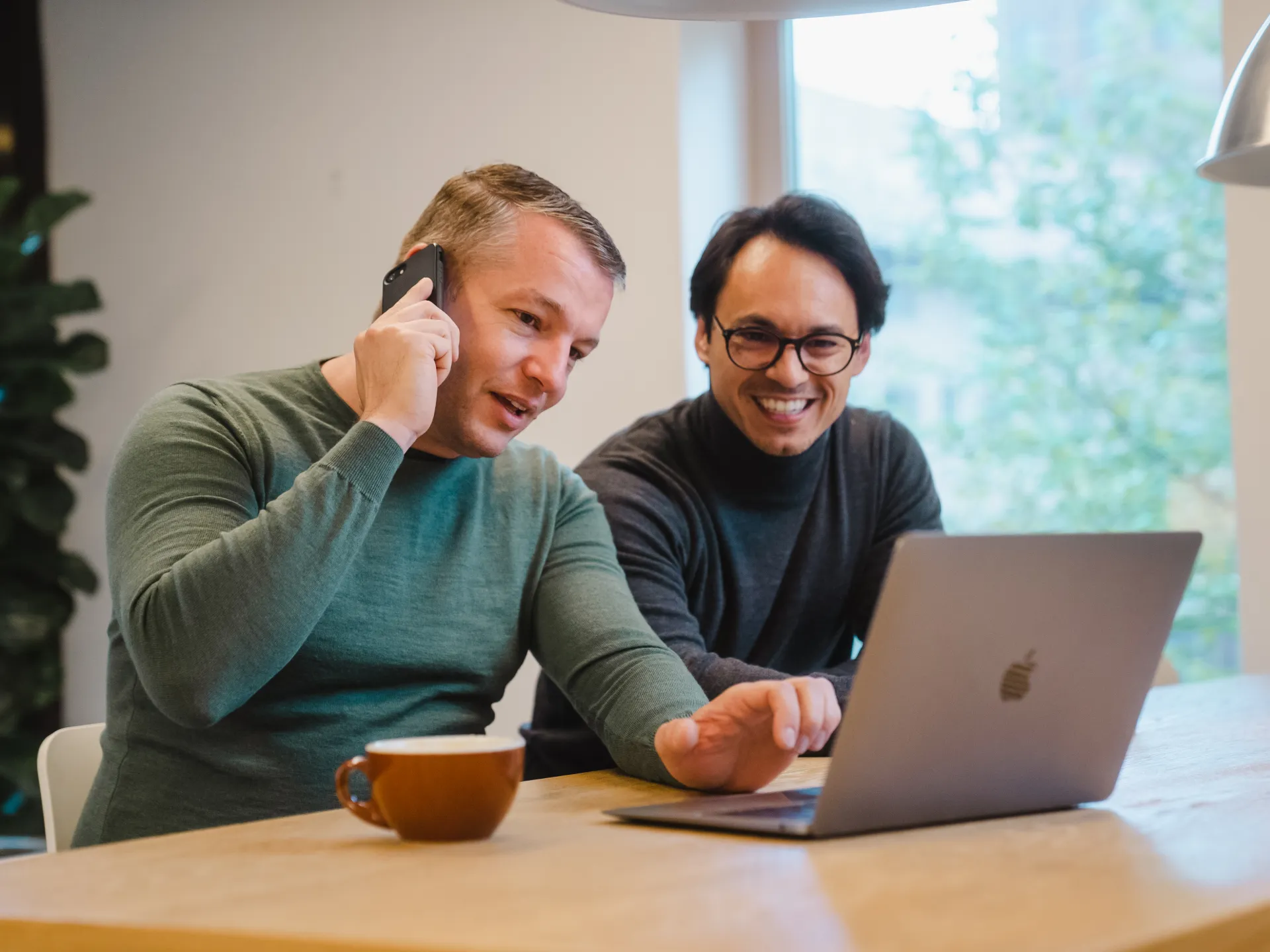 Twee adviseurs overleggen telefonisch en achter de laptop aan een kantoortafel